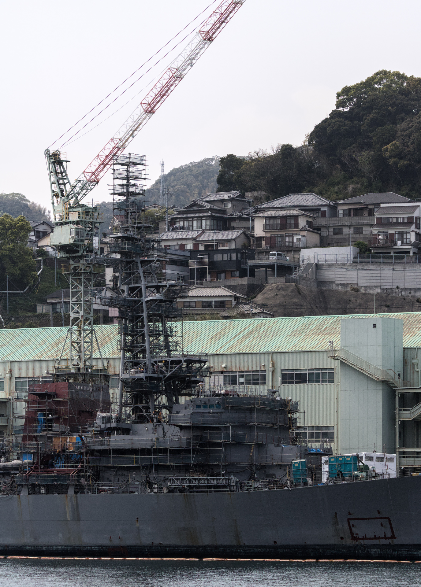 Docked military ship with houses stacked on the mountain behind it.